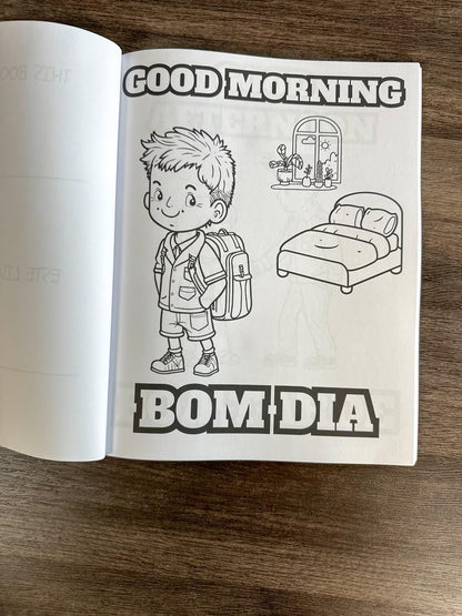Open book with a coloring page of a child and 'Good Morning Bom Dia' text on a wooden surface. How To Cook Portuguese Stuff coloring book. 

