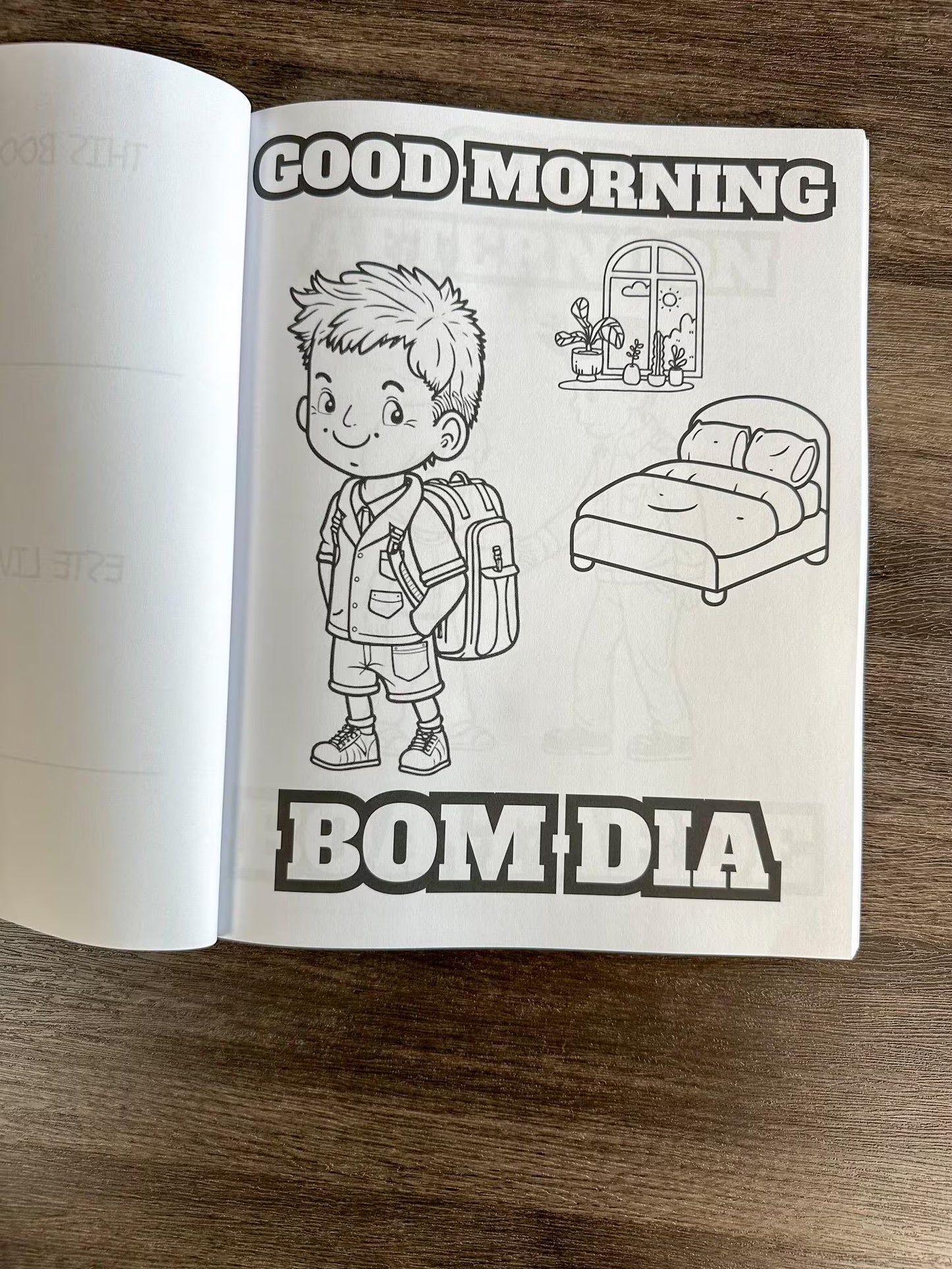 Open book with a coloring page of a child and 'Good Morning Bom Dia' text on a wooden surface.

