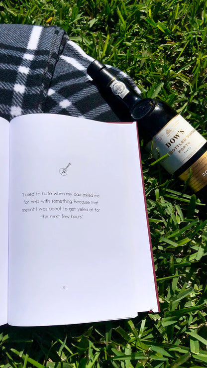 Open book with text on grass next to a bottle of wine

